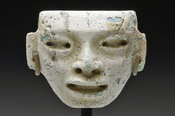 Pre-Columbian, Eastern Mexico, Ca 200 to 600 CE. Carved stone head, in what looks to be turquoise, now covered in deep white caliche (hardened deposit of calcium carbonate); with deep set, almond-shaped eyes, large lips open as if speaking and drilled ears. Custom stand. 20mm x 23mm. PROVENANCE: Ex-prominent Chicago, IL Collection acquired from Throckmorten Fine Arts. Authenticity Guaranteed