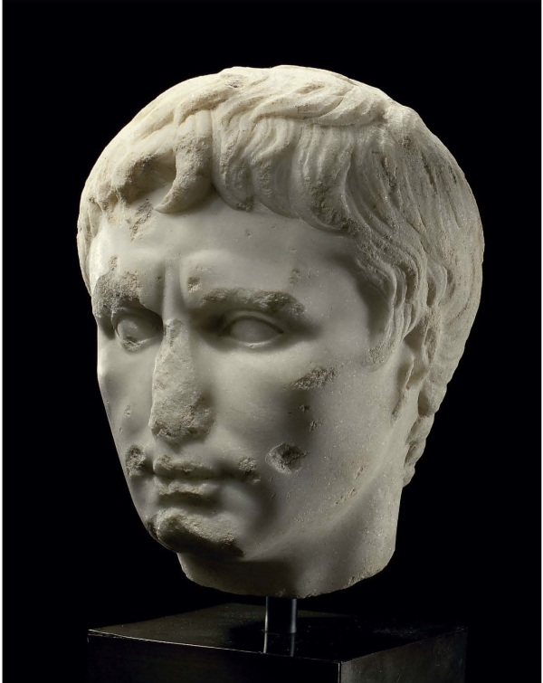 Lot 114. A ROMAN MARBLE PORTRAIT HEAD OF THE EMPEROR AUGUSTUS  CIRCA LATE 1ST CENTURY B.C.-EARLY 1ST CENTURY A.D.  Over-lifesized, depicted with finely-modelled features, his oval face with strong cheekbones, the fleshy bow-shaped mouth with the lips pressed together, dimpled at the corners, the philtrum indicated, the naso-labial folds subtly portrayed, his almond-shaped convex eyes unarticulated and slightly recessed, two small diagonal lines extending above the bridge of his nose accentuating his knitted brow, a single shallow crease across the broad forehead, the layered hair composed of a mass of short comma-shaped locks, with the three characteristic locks at the center of his forehead, two parted at the center and one to his right, a single lock curving forward before each ear 12½ in. (31.8 cm.) high  Estimate: $200,000-250,000. Click on image to enlarge. Provenance Enrico Serranti and Giovanna LoMoro, New York and New Jersey, acquired in 1981. with Fortuna Fine Arts, New York, 1999. Antiquities, Christie's, New York, 8 June 2004, lot 57. 